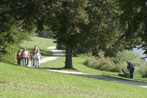 Eine Gruppe Wanderer wandert entlang eines Wanderwegs vorbei an grünen Wiesen und Bäumen.