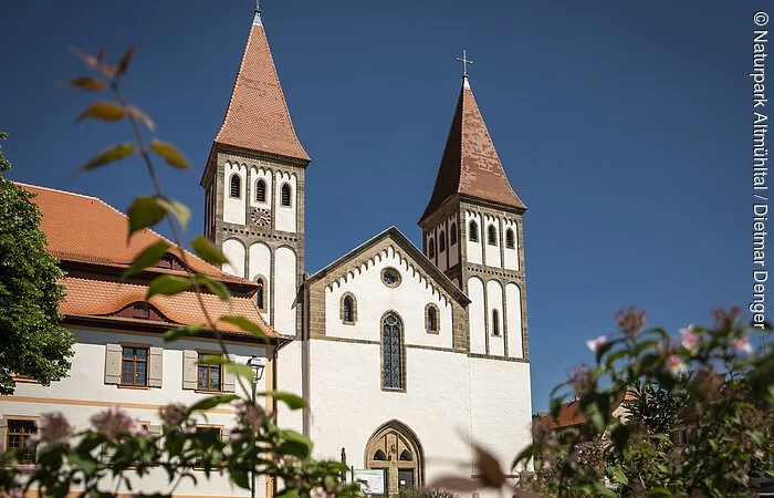 Das Kloster mit seinen zwei Türmen inmitten grüner Büsche. Der Himmel strahlt wolkenlos.